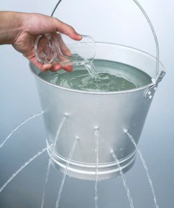 Hand pouring water from a glass into a leaking pail 